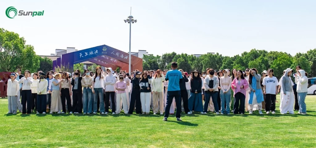 A large group of Sunpal employees standing on a green field listening to a speaker.