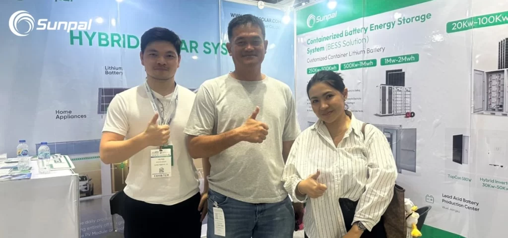 Three people giving thumbs up at the Sunpal solar exhibit booth with hybrid solar system displays.