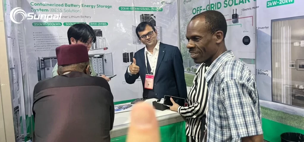 Visitors and Sunpal reps talking at a trade‑show booth with battery storage and off‑grid displays; one rep giving a thumbs up.