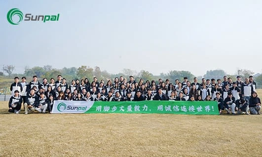 Large Sunpal team posed outdoors on grass holding a long green banner under a pale sky.