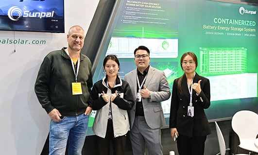 Four people posing at the Sunpal booth in front of a green display about containerized battery storage and on‑grid solutions.