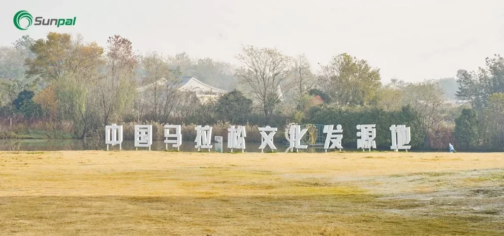 Wide view of a grassy field with large white Chinese characters near a tree line; Sunpal logo in the corner.